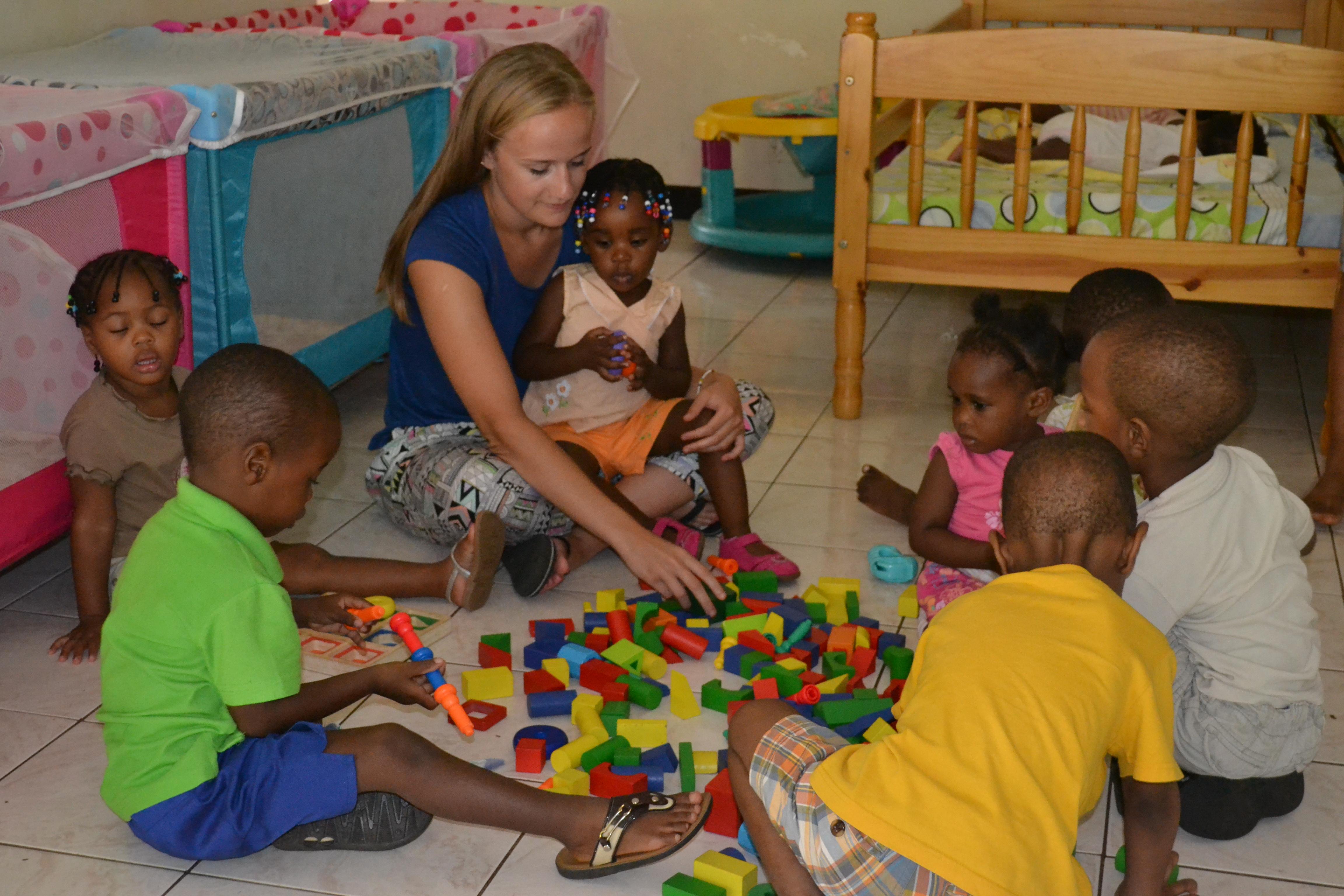 Projects Abroad Childcare volunteer helps a group of children learn through play with building blocks at a daycare centre. Under the guidance of Projects Abroad volunteers working with children in Jamaica, a group of kids play with building blocks at a daycare centre.